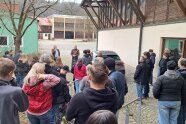 Personen stehen im Freien neben einem landwirtschaftlichen Gebäude