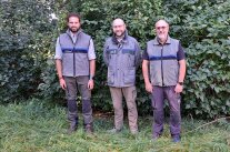 Drei Personen in Forstkleidung vor einer Hecke